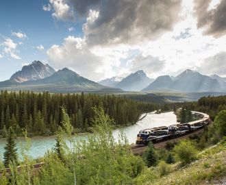 Toget Rocky Mountaineer som snor sig langs flod i Canada med Rocky Mountains i baggrunden