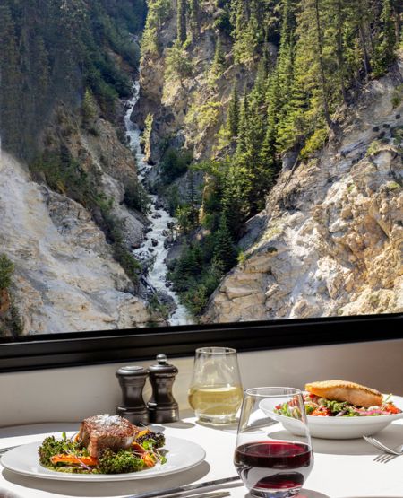 Middag med hvid dug og udsigt til bjerglandskab ombord på luksustoget Rocky Mountaineer i Canada