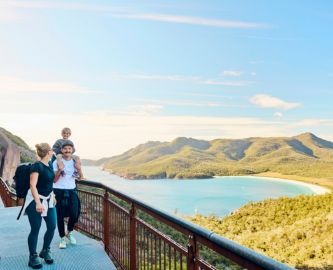 Familie på tre går langs boardwalk med udsigt over bugt på Tasmanien