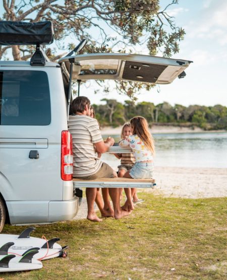 Børnefamilie spiser frokost i bagenden af autocamper med udsigt til sø i Australien
