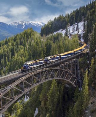 Rocky Mountaineer kører over stålbro i bjergrigt canadisk landskab
