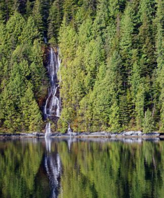 Vandfald, som falder over bjergskråning omgivet af nåletræer langs Canadas kyst