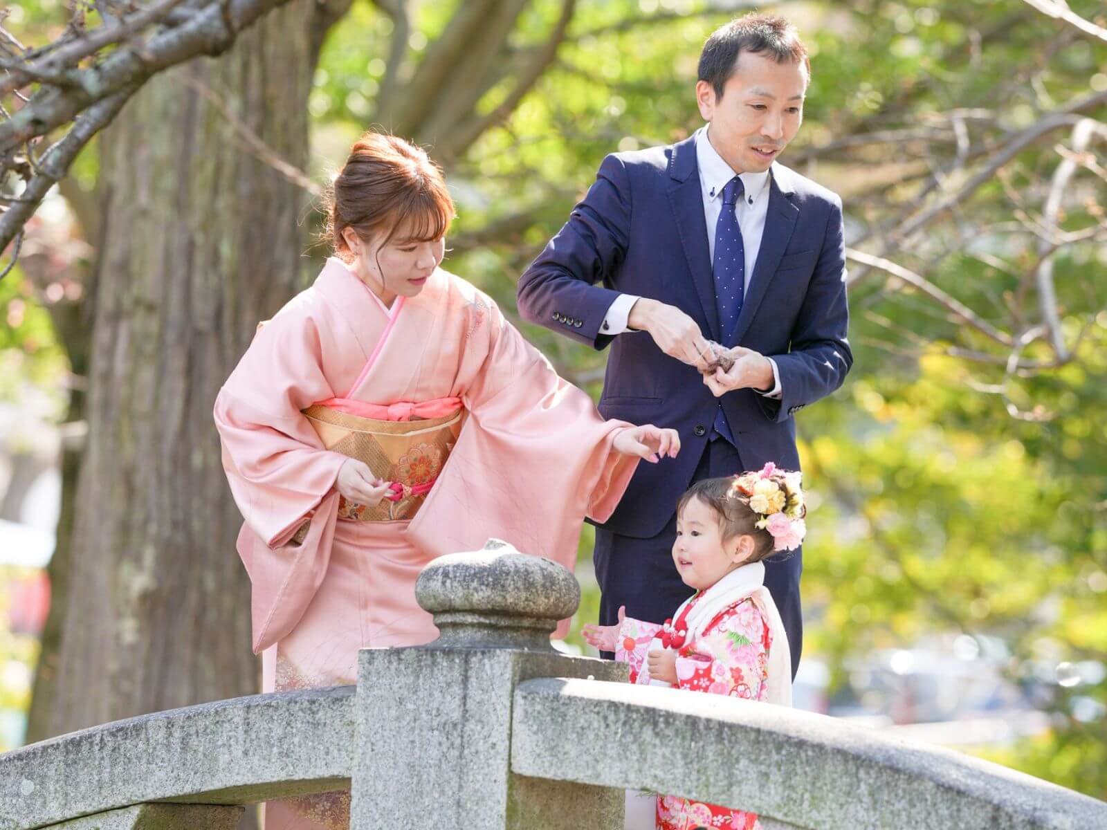 Lille japansk familie på stenbro. Mor og barn i traditionel japansk geishadragt og far i vestligt jakkesæt, Japan