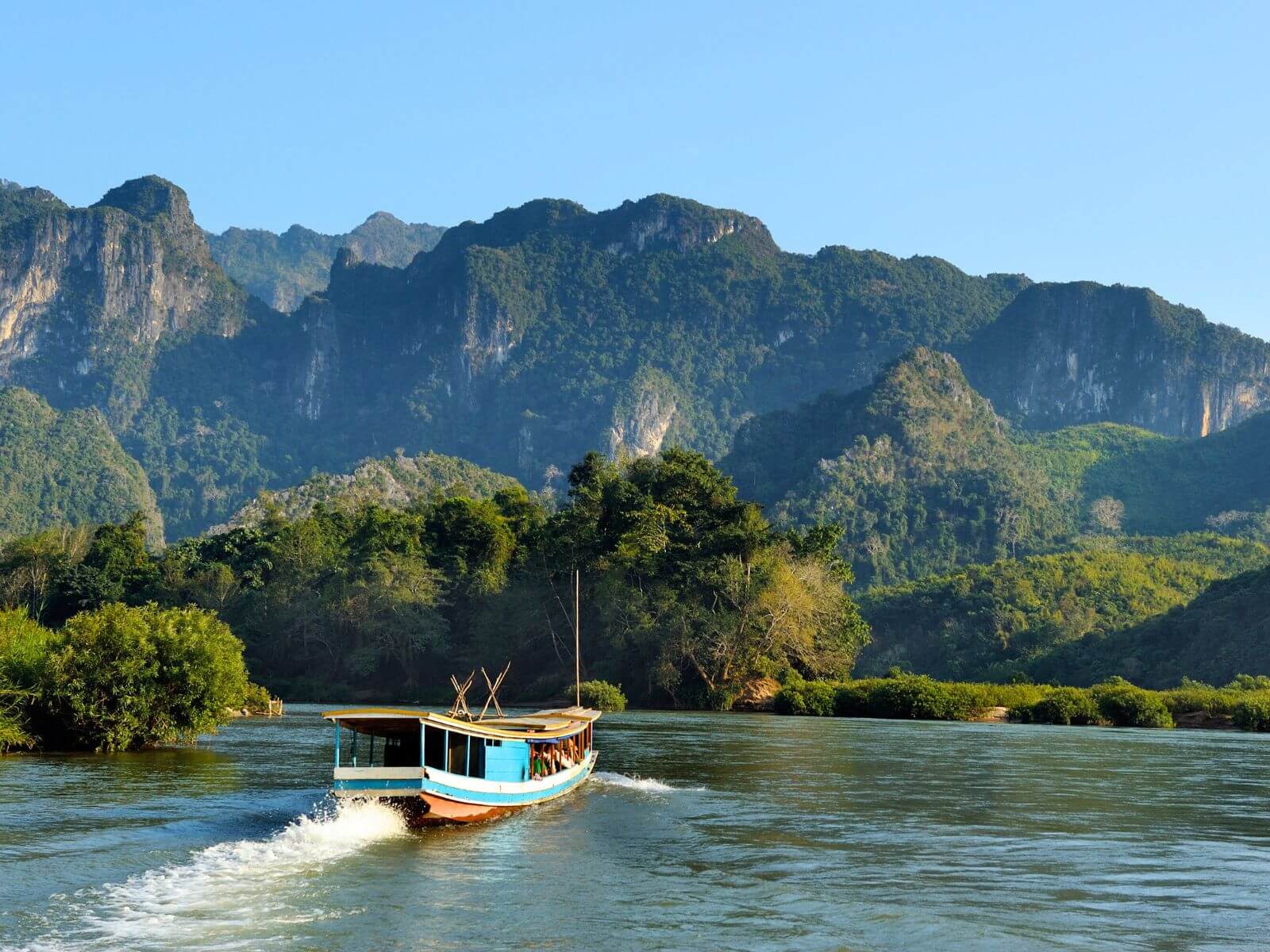 Turistbåd på Mekong-floden i Laos, nær Luang Prabang, med med udsigt til blå himmel og grønne bjerge Turistbåd på Mekong-floden i Laos, nær Luang Prabang, med med udsigt til blå himmel og grønne bjerge