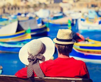 Par som sidder og kigger ud over havn med farverige både på Malta