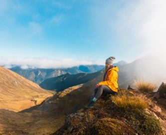 Kvinde i guk jakke hviler i bjergrigt landskab efter vandretur i New Zealand