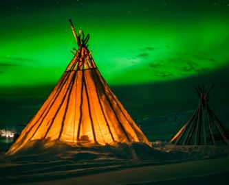 Oplyst Lavvo-telt med nordlys på himlen