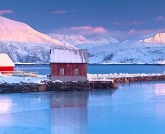 Udsigt til rødt fiskerhus, fjord og sneklædte fjelde