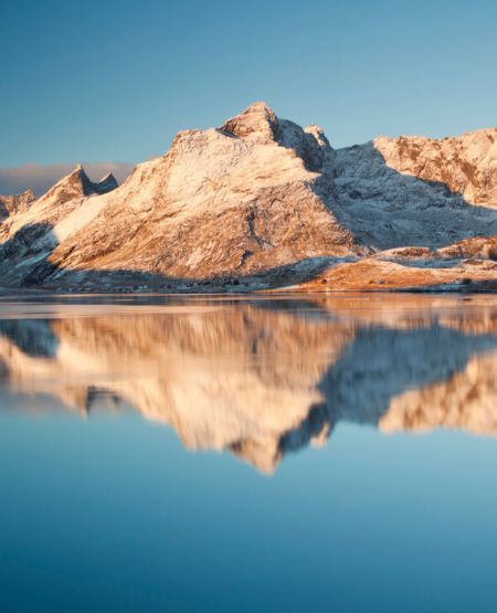 Udsigt til Lofotens flotte sneklædte klippekyster med fjord og blå himmel