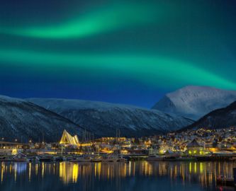 Udsigt over Tromsø oplyst af aftenlys og nordlys