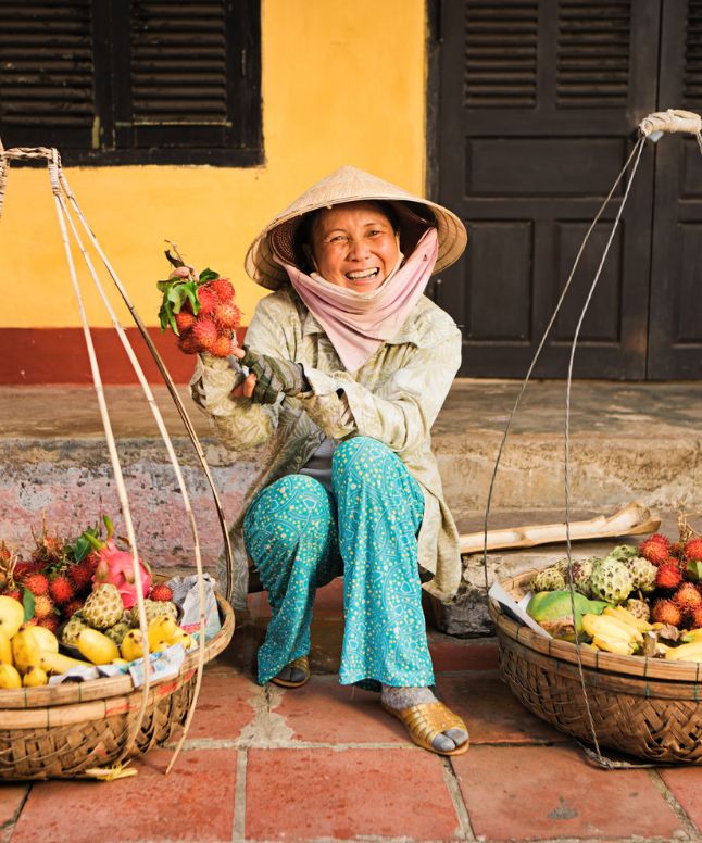Smilende vietnamesisk kvinde, der viser grøntsager frem