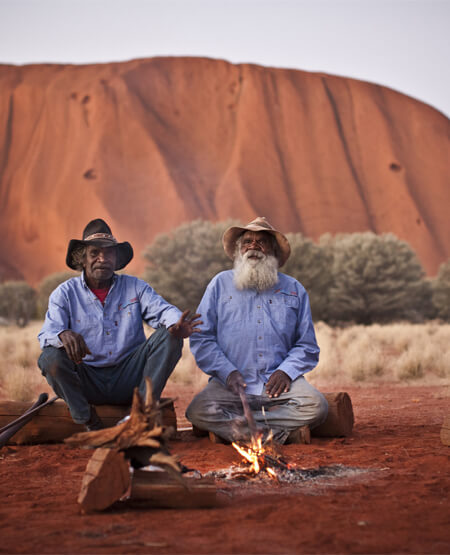 Aboriginale som sidder foran Ayers Rock Uluru i Australien