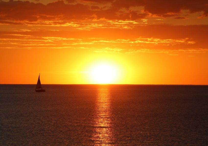 Solnedgang over havet og sejlbåd i horisonten