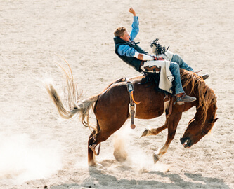 Western-rytter på vild hest i sand der støver op i Calgary