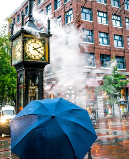 Menneske bag paraply kigger på det berømte Steam Clock i Vancouvers gastown