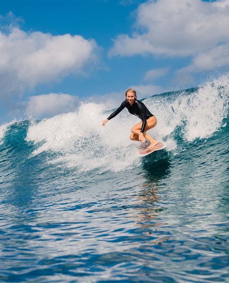 Kvinde som surfer i høje bølger i Seminyak på Bali