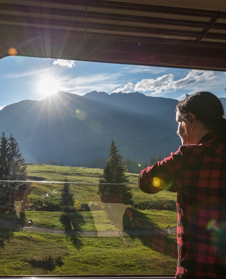 Kvinde kigger ud på bjergrig natur via et togvindue Kvinde kigger ud på bjergrig natur via et togvindue