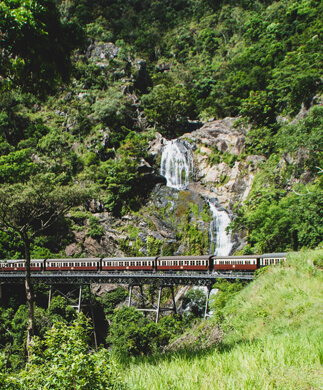 Udsigt over tog der kører forbi skov og vandfald på Kuranda i Australien