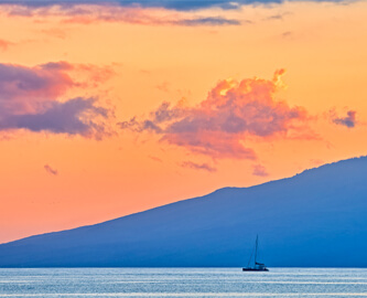 Solnedgang over hav, skib og bjerg på Hawaii